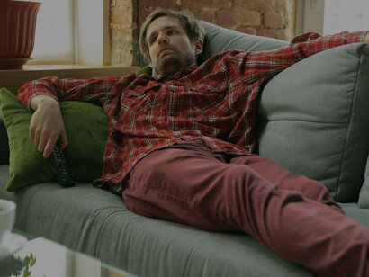 A young man lying on the sofa at home exemplifies the laziness encouraged by modern convenience culture