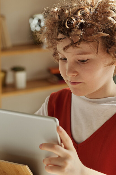 Criança no período escolar manuseando um equipamento eletrônico para realizar atividades de aula