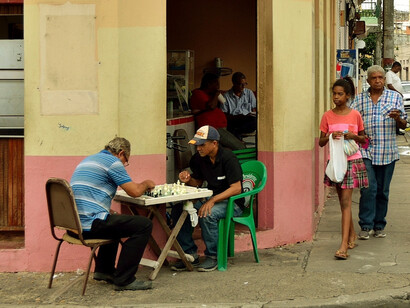 The streets come alive with the rhythmic clack of domino tiles in Santo Domingo, amidst the honking cars and bachata melodies, locals gather at 'colmados' for an evening of fierce gameplay and camaraderie