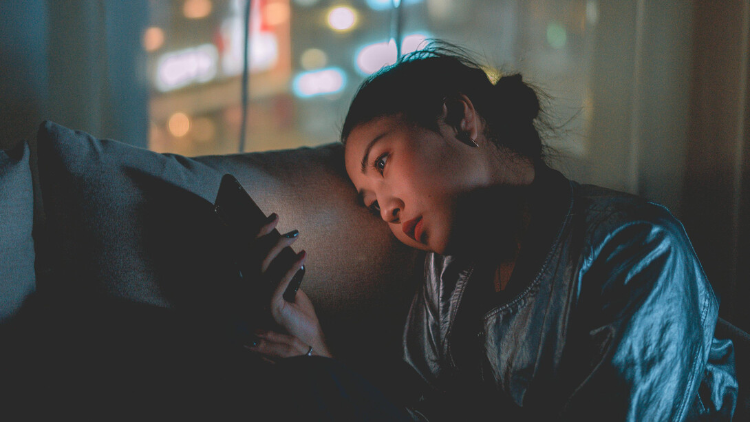 A woman lying on a pillow looking at her phone with sadness