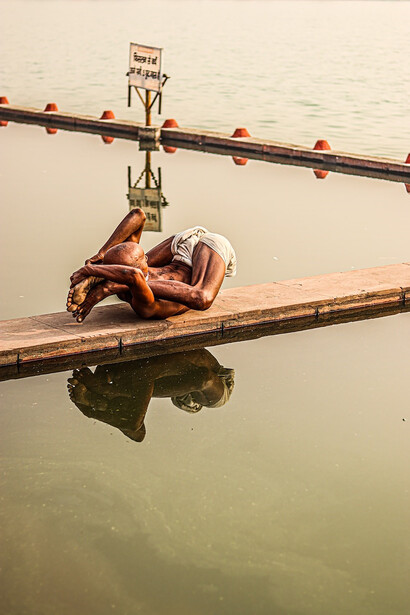 A man is peacefully laying on a wooden dock next to a serene body of water, engaging in yoga asanas and performing exercises that invigorate his body, channeling a sense of vibrant energy