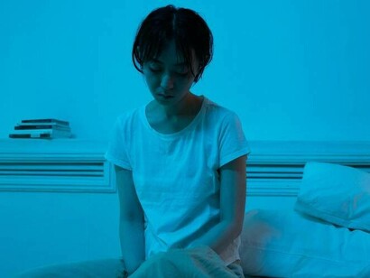 A woman looking depressed as she sits on her bed and stares at her bed sheets