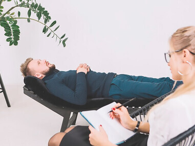 Discover the holistic healing approach as a female psychologist takes meticulous notes in her diary while her patient reclines on a couch in the clinic, promoting mental wellness through personalized care