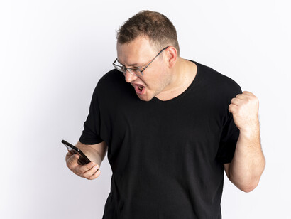 A man in a black shirt screaming in rage at his cellphone