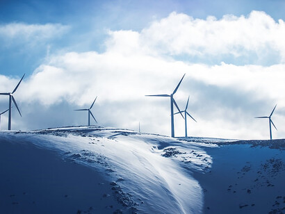 Amidst a snowy landscape, windmills stand tall against the daytime sky, creating a harmonious blend of renewable energy and serene winter beauty