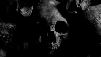 Human skulls emerging from shadow, representing history’s refusal to remain buried