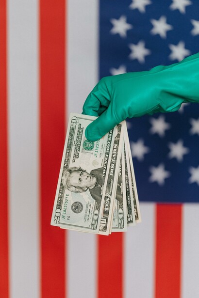 Person holding American dollars with gloves in front of the American flag