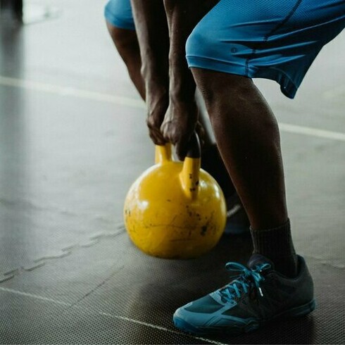 A man lifting a kettlebell, a reminder that maintaining a consistent fitness routine not only enhances physical health but also promotes mental well-being, resilience, and longevity