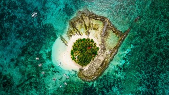 An aerial view of Guyam Island in Siargao, signifying the timeless allure of small islands surrounded by vast seas