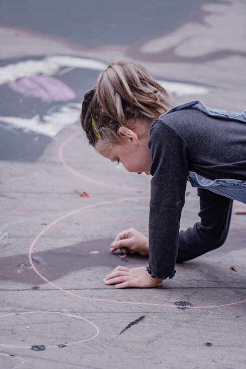 The playground transforms into a nostalgic playground as the young girl sketches out her hopscotch grid, ready to revive a cherished game that has delighted children for centuries