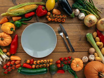 A empty plate besides a knife and a fork, between assorted vegetables on a table