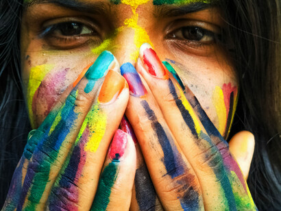 A woman covers her mouth and nose with her hands, staring at the camera, smeared with paint