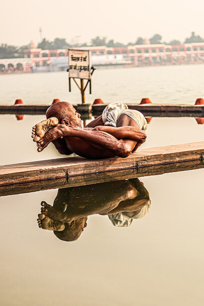 Beside a tranquil body of water, a man rests on a wooden dock, practicing yoga asanas and performing exercises that infuse his body with revitalizing energy