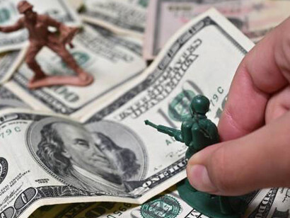 Person hand playing with team of classic life size toy soldiers shooting an enemy on dollar notes