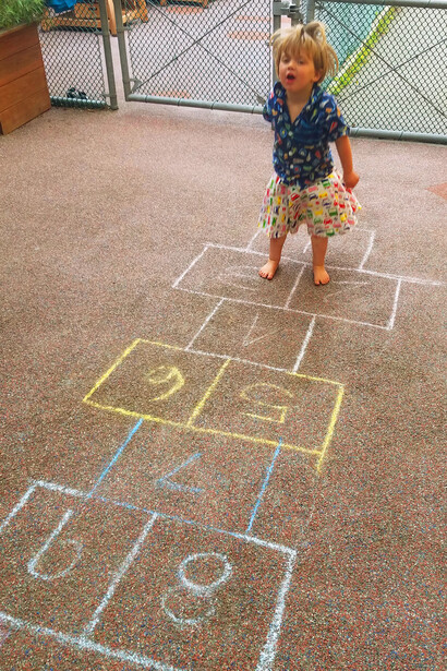 As she navigates the hopscotch grid with boundless energy, the young girl brings to life a cherished memory, celebrating a game that has been a bridge between generations