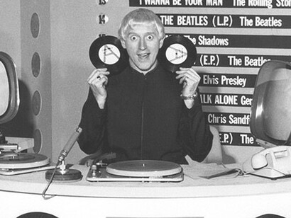 In this captivating photo, a DJ from the past proudly showcases his collection of plaques, surrounded by an iconic old-school DJ machine