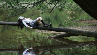 A woman lying on a tree branch near the water