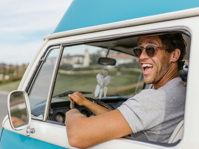 A man in glasses driving a van, smiling