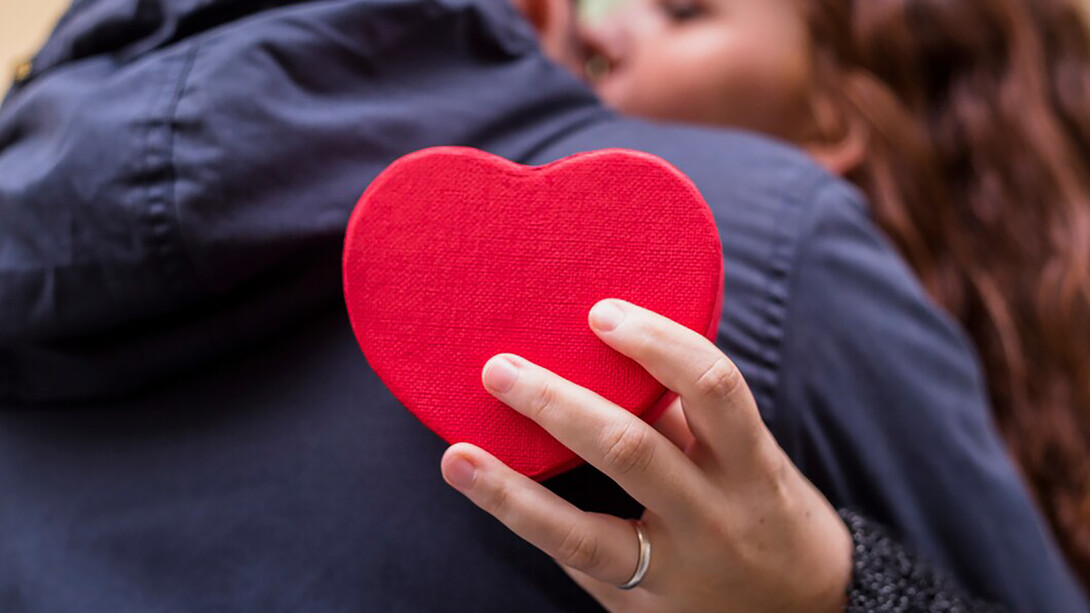 A woman embraces a man while holding a heart-shaped gift box