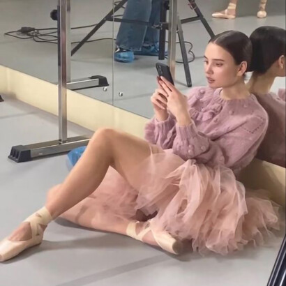 A ballet dancer sits on the floor, engrossed in her phone