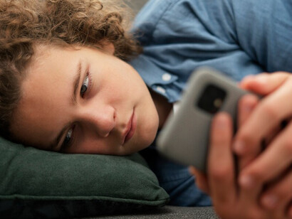 A young man with a distressed expression, staring at his phone, illustrating the stress of negative news consumption