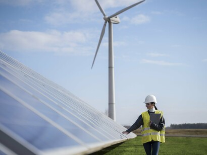 A woman working on a field of solar panels and towering wind turbines that harness the power of the sun and wind and generate clean, renewable electricity