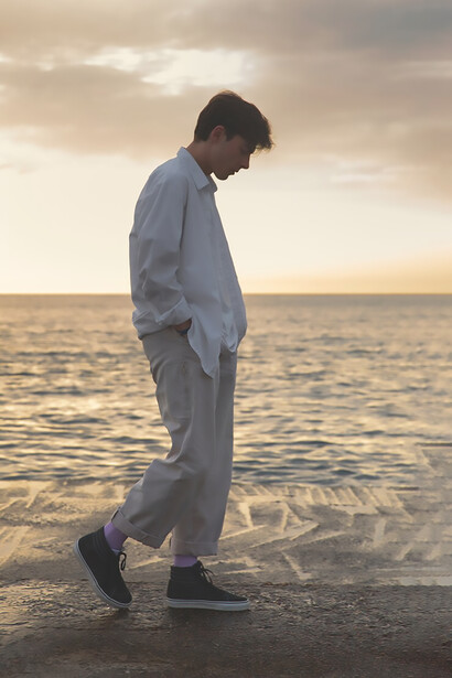 Silhouetted against the sunset by the sea, a man stands lost in thought, the rhythmic waves echoing the depth of his contemplation