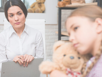 Close-up of a female therapist supporting a distraught girl with a teddy bear during a therapy session, illustrating emotional dysregulation