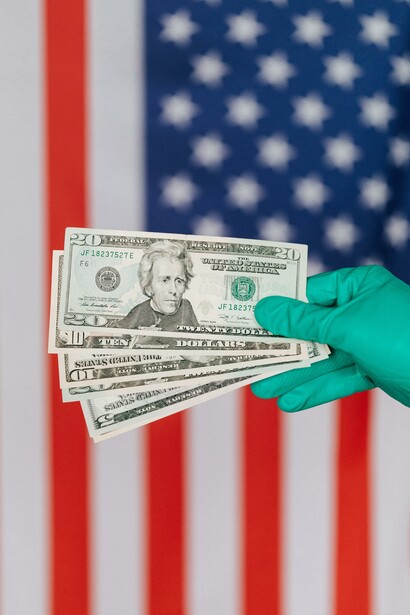 Person holding American dollars with gloves in front of the American flag