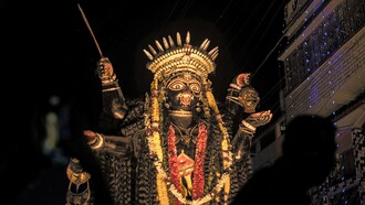 Uma visão noturna detalhada de uma representação da deusa hindu Kali lindamente adornada, iluminada com luzes festivas