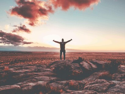 A man with arms stretched wide open in the middle of a field in the sunset is feeling the changes and expressing his gratitude