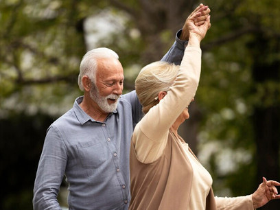 A happy, elderly couple dancing in the park represents the benefits of physical health, a positive lifestyle, and healthy living