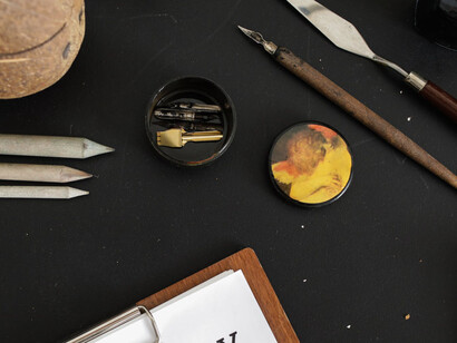 Tavolo di lavoro con pennelli, matite e spatole: l’immagine che si forma appare come uno scomposto miscuglio di lettere