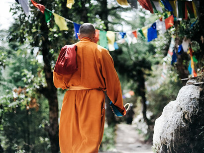 A serene figure in crimson robes, a monk walks the ancient trails of Nepal, embodying tranquility amidst the majestic yet challenging Himalayan landscape