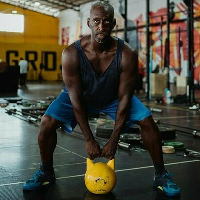 A determined man in a gym setting lifts a yellow kettlebell, emphasizing the crucial role of regular exercise in maintaining physical strength, enhancing overall health, and supporting a consistent fitness routine for long-term wellness