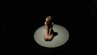 Uma mulher ajoelhada sob um único holofote, cercada pela escuridão. Às vezes, o confronto mais difícil acontece quando não há ninguém por perto além de nós mesmos