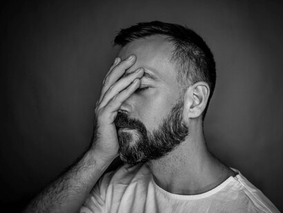 A man covering his eyes with his hand as he tries to manage his stress levels