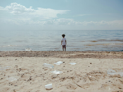 A child stands on the shore in a dirty beach