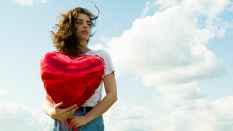 A woman holding a heart-shaped balloon beneath an open sky, representing the ability to protect one's heart without closing it off