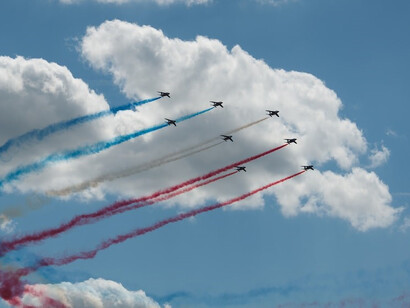 Aircrafts creating contrails of blue, red, and white as it soars through the skies above Circuit Le Mans in Le Mans, France
