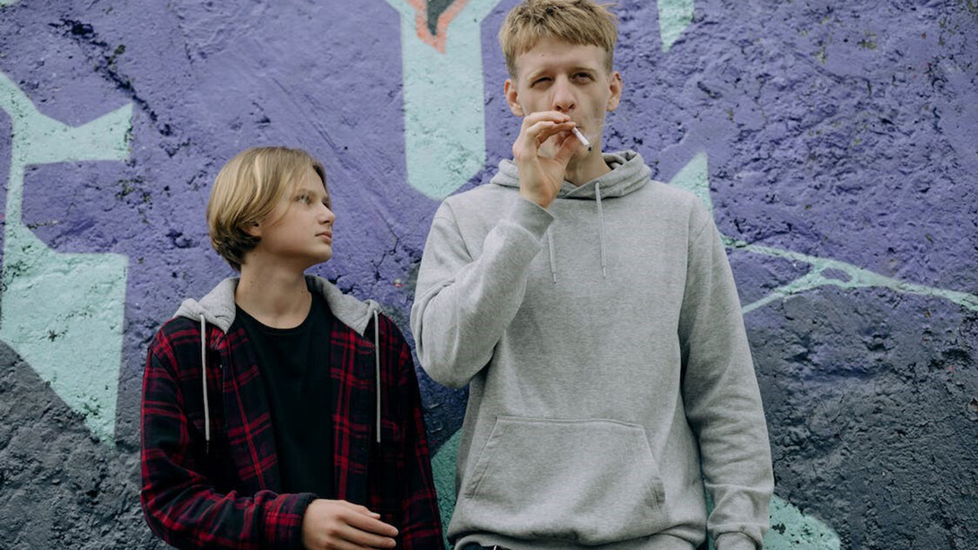 Two teenagers, one puffing on a cigarette while the other patiently waits for their turn