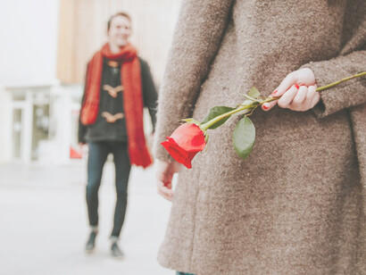 A woman waits for a man while holding a rose
