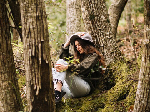 Sitting on a tree in a serene natural setting, a young woman holds a camera, embracing the quiet moments that inspire stillness and mindfulness