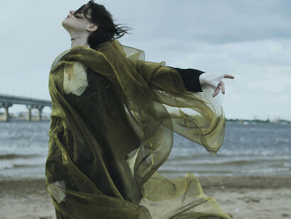 A woman with a long green shawl on the beach facing the wind