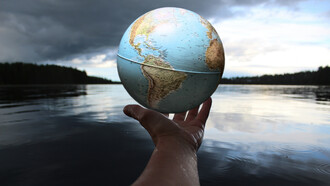 Entre ombre et lumière, un globe tenu à la main rappelle une évidence : la mondialisation ne disparaît pas, mais se redéfinit, entre tensions géopolitiques et interdépendances inévitables