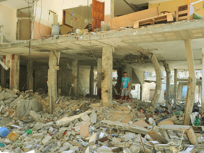 Surrounded by the remnants of war, he represents the voices advocating for a culture of peace, emphasizing that peace must be fought for, even in the darkest times