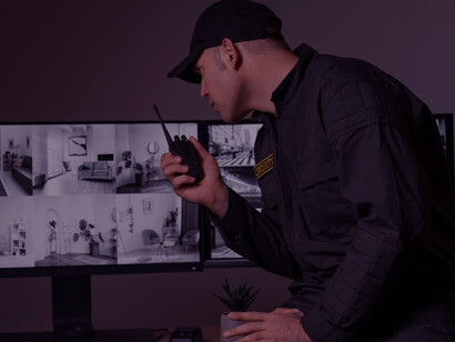 A portrait of a male security guard overseeing radio communications and surveillance camera screens