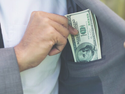 A man in a suit pockets cash, symbolizing corruption