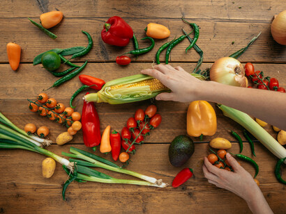 A human hand reaching for a piece of corn between assorted vegetables on a table