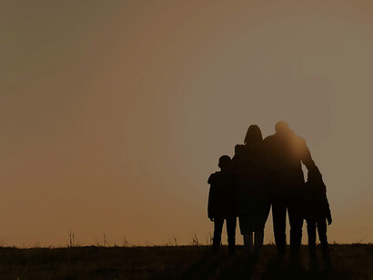 Against the backdrop of a radiant sunset, a full-shot silhouette portrays a joyous family reveling in moments of fun and togetherness